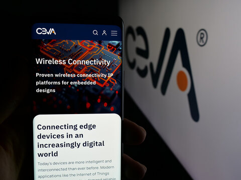 Stuttgart, Germany - 11-14-2025: Person holding cellphone with webpage of US semiconductor company Ceva Inc. on screen in front of logo. Focus on center of phone display.