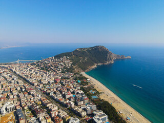 Wide aerial panorama of the dense urban area of Alanya, the mountainous peninsula, and the long stretch of beach meeting the turquoise Mediterranean Sea