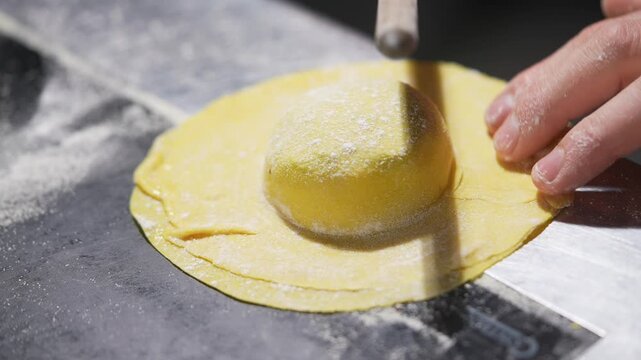 A person is making a yellow doughnut on a table. The doughnut is being rolled out with a wooden rolling pin