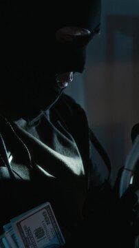 Vertical tilt up shot of young criminal enjoying smell of stolen cash and smugly nodding his head up and down in dim light
