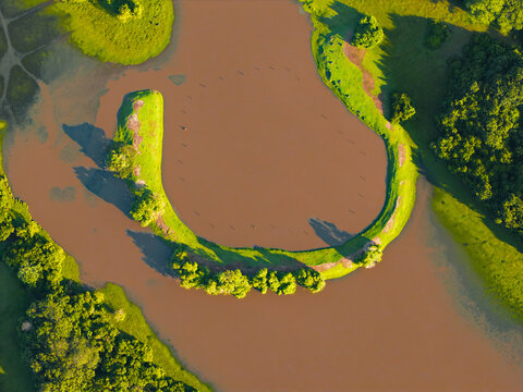 Aerial view of the winding Guanapalo River cutting through vibrant green grasslands, creating a striking contrast of earth tones and verdant life, San Luis de Palenque, Casanare, Colombia.