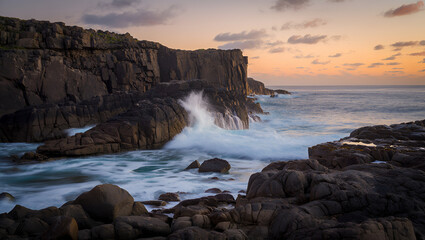 Powerful ocean waves crashing against rugged dark cliffs at a vibrant sunset