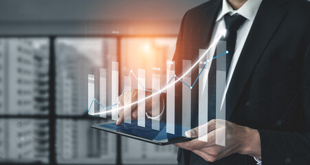 A professional man analyzes data trends using a tablet in a modern office environment. The upward graph represents business growth and success. Impute