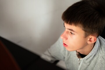 Deep in thought, a teenager contemplates ideas while seated at a table in a cozy, minimalist room during the soft afternoon light