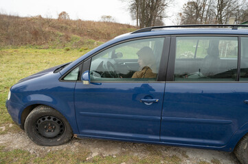 Family outing to the countryside in early spring with a blue minivan parked on a grassy meadow while passengers enjoy the fresh air and scenic views