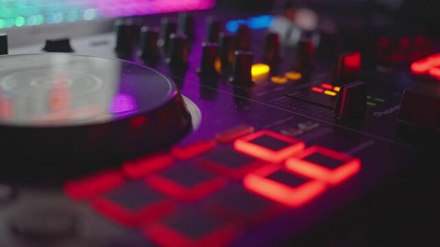 studio pad illumination, electronic music setup with glowing control surfaces and jog wheel, closeup of illuminated controls on modern electronic music production hardware in lowlit studio environment