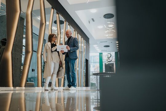 Two professionals review a document in a sleek, contemporary lobby with glass and warm lighting, signaling collaboration and a productive business discussion.