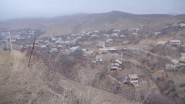 View from a moving vehicle showing a lake with a water tower in rainy weather and a winding mountain road with a sharp turn warning sign.


