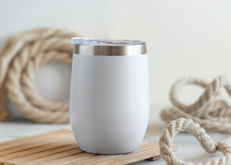 White blank Stainless Steel tumbler on wood against rustic jute ropes close up, nautical mockup © katrinshine