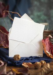 Card on wood near autumn dried leaves closeup, wedding and party mockup in blue, red and orange