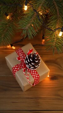 caja de regalo decorada con un lazo sobre una mesa de madera, acompa&ntilde;ada de una rama de pino, una pi&ntilde;a y luces navide&ntilde;as encendidas que crean un ambiente festivo y c&aacute;lido.