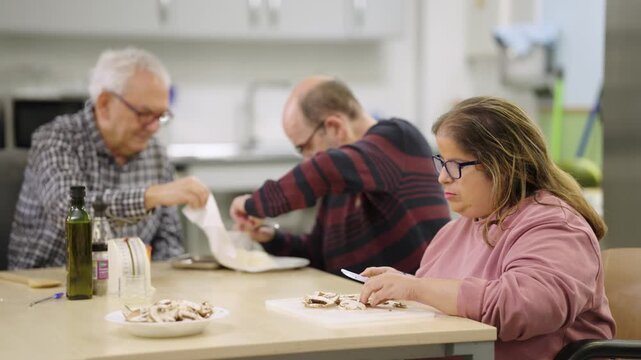 Group of people with disabilities participating in a cooking class. A woman in a wheelchair is cutting mushrooms on a cutting board