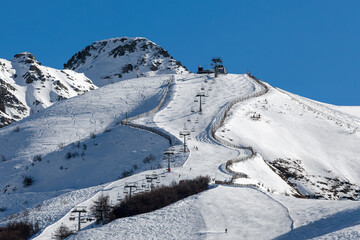 Scenic winter landscape of a snowy alpine ski slope surrounded by rugged mountain peaks under a clear blue sky in Italy.