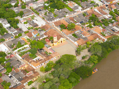 Aerial view of terracotta roofs meet verdant trees and the ochre-colored church square, a vibrant tapestry woven by the river's edge, Mompox, Bolivar, Colombia