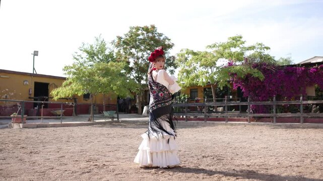 Beautiful woman in traditional white dress and black shawl dancing flamenco in a sandy courtyard. Her passionate performance embodies spanish culture