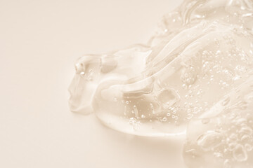 Close-up shot of beige liquid cosmetic gel or serum makeup swatches with a glossy, shiny texture on a smooth beige background.