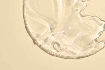 Close-up shot of beige liquid cosmetic gel or serum makeup swatches with a glossy, shiny texture on a smooth beige background.