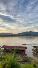 Traditional houseboats and small motorboats on the Mekong River, showcasing local riverside life against a backdrop of mountains and a clear blue sky.