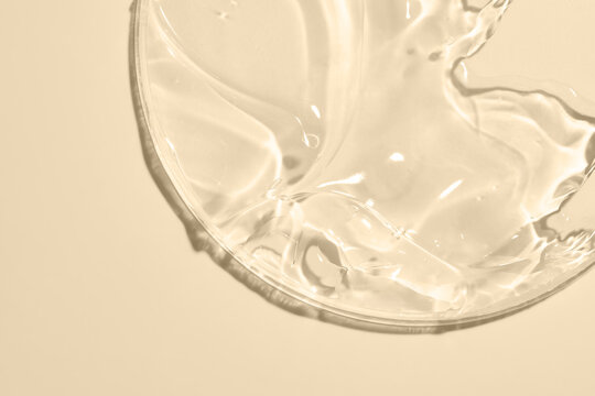 Close-up shot of beige liquid cosmetic gel or serum makeup swatches with a glossy, shiny texture on a smooth beige background.
