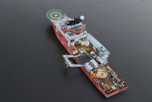 Aerial view of the vibrant red and white service vessel cutting through the dark water, contrasting with the helipad's stark circle, Poughkeepsie, New York, United States.