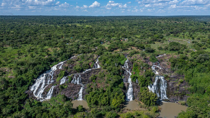 Aerial view of cascading waterfalls plunging down rocky cliffs amidst a lush, verdant forest canopy, Aruu water falls, Northern Region, Uganda.