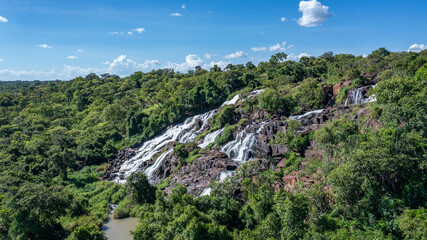 Aerial view of cascading waterfalls plunge down rocky cliffs, embraced by verdant forests under a vast sky, Aruu water falls, Northern Region, Uganda.