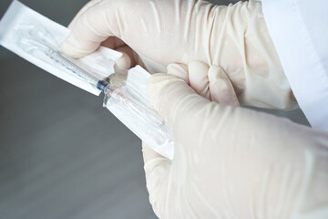 Gloved hands holding syringe in packaging for safe medical administration preparation.