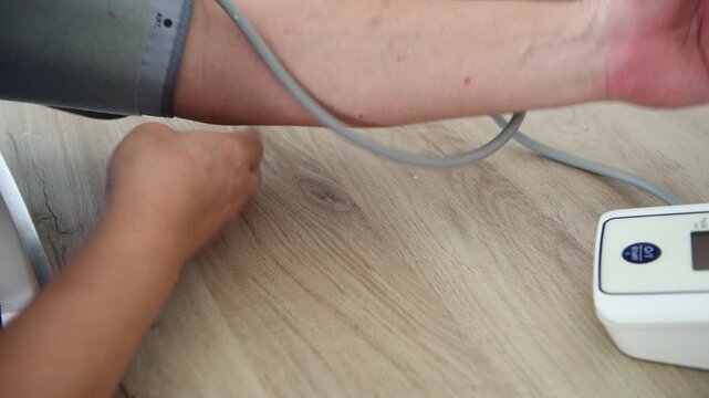Close up of a person fitting the inflation cuff of a blood pressure monitor on the arm and pressing the start button to measure blood pressure.