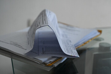 stack of documents on glass desk, curled paper detail, bureaucracy and stress business paperwork pile, office environment, information overload concept financial or legal forms, abstract view of paper