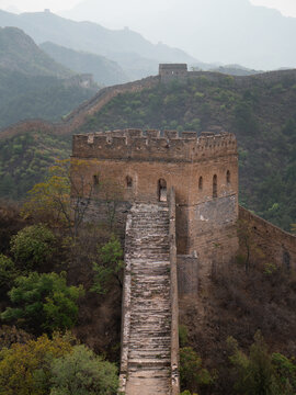 View of ancient stone steps ascend towards a formidable watchtower along the Great Wall, nestled amidst misty mountains, Beijing, Beijing, China.