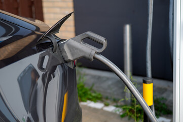 A partial view of an electric car with a plug connected during charging, showing the recharging process, growth of urban infrastructure, and adoption of modern eco-friendly technologies in transport