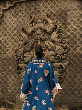 Jinzhong, China - 30 October 2025: View of a woman in traditional blue attire gazing at the intricate carvings of the Wang Family Compound, with its textured stone and ornate details.