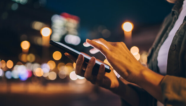woman is using touching smartphone display outdoors. Blurred city night background