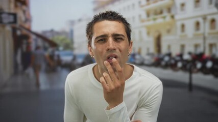 Young man in white shirt with pensive expression standing on a bustling street in an urban cityscape