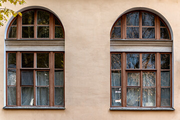 Two arched windows with old brown wooden frames against a light brown wall. From the Mira window series.
