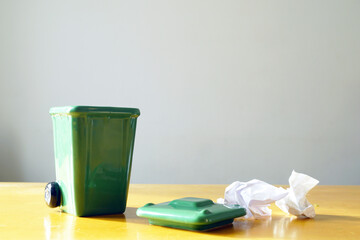 Miniature green waste bin with lid and crumpled paper trash on a light background. Represents creative process, idea refinement, productivity workflow, workspace minimalism, and planning visuals. 