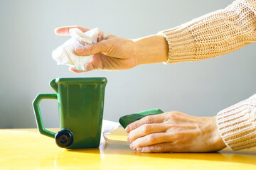 Hand throwing crumpled paper toward a miniature green waste bin. Represents waste disposal action, environmental habit practice, trash sorting engagement, and sustainability education process.