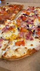 Slice of pizza topped with cheese, ham, tomatoes, and onions on cardboard box background