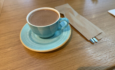 Hot chocolate in blue cup on wooden table background with utensils for cozy cafe setting