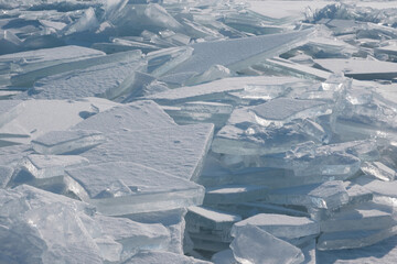 The accumulation of large, transparent, and snow-covered blocks of ice in winter is likely on a frozen lake or sea. The ice is broken into many sharp fragments illuminated by bright sunlight.