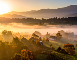 Sunrise illuminates fog covered village in a serene rural landscape with golden morning light