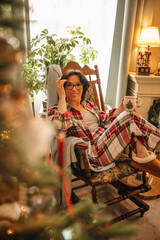 A woman in a checkered pyjama is drinking tea in a Christmas interior