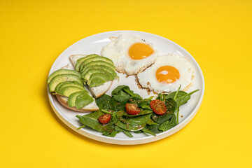 Healthy breakfast with fried eggs avocado and spinach salad