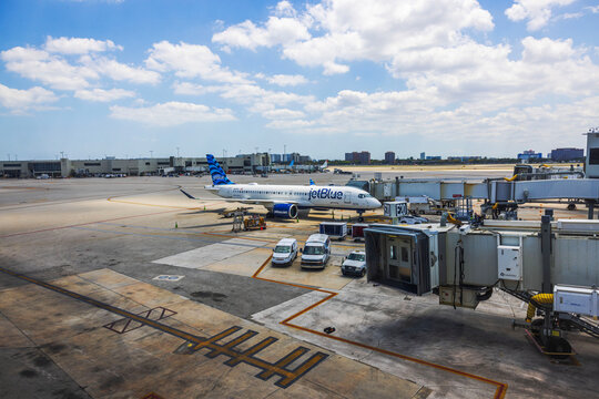 Beautiful view of Jet Blue airplane parked at airport gate with service vehicles and jet bridge. Miami. USA.