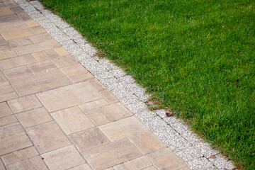 Paved walkway with gravel edge bordering lush green lawn. Landscape design, property maintenance, hardscape transition. Real photo.