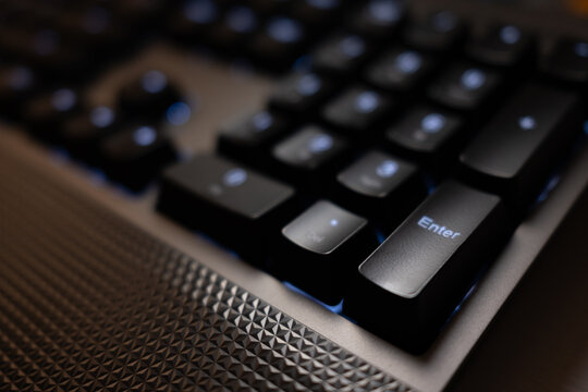 Close-up of the 'Enter' key on a modern black gaming keyboard with blue LED backlighting. The shallow depth of field highlights the textured surface and high-tech design.