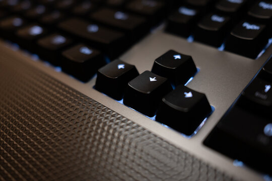 Close-up of arrow keys on a modern black keyboard with blue LED backlighting. The textured surface and shallow depth of field create a high-tech, futuristic feel.