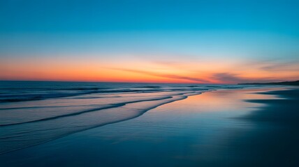 Ocean waves washing onto sandy beach reflecting sunset colors in the water