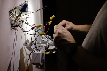 Hands working on electrical wires in a dimly lit room during home repair