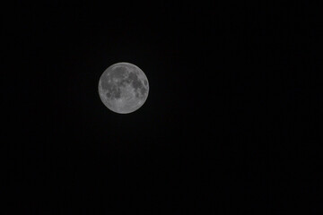 Macro shot of a full moon set against a clear, dark night sky. The moon is detailed, with clearly visible craters and maria on its surface